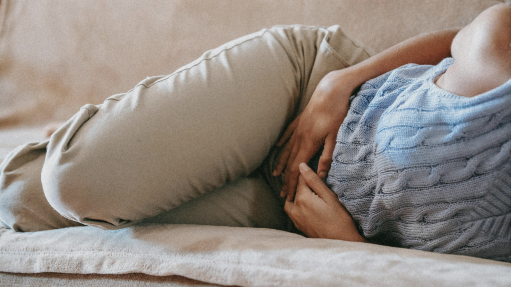 Woman sitting on a couch holding her pelvic area with a painful expression